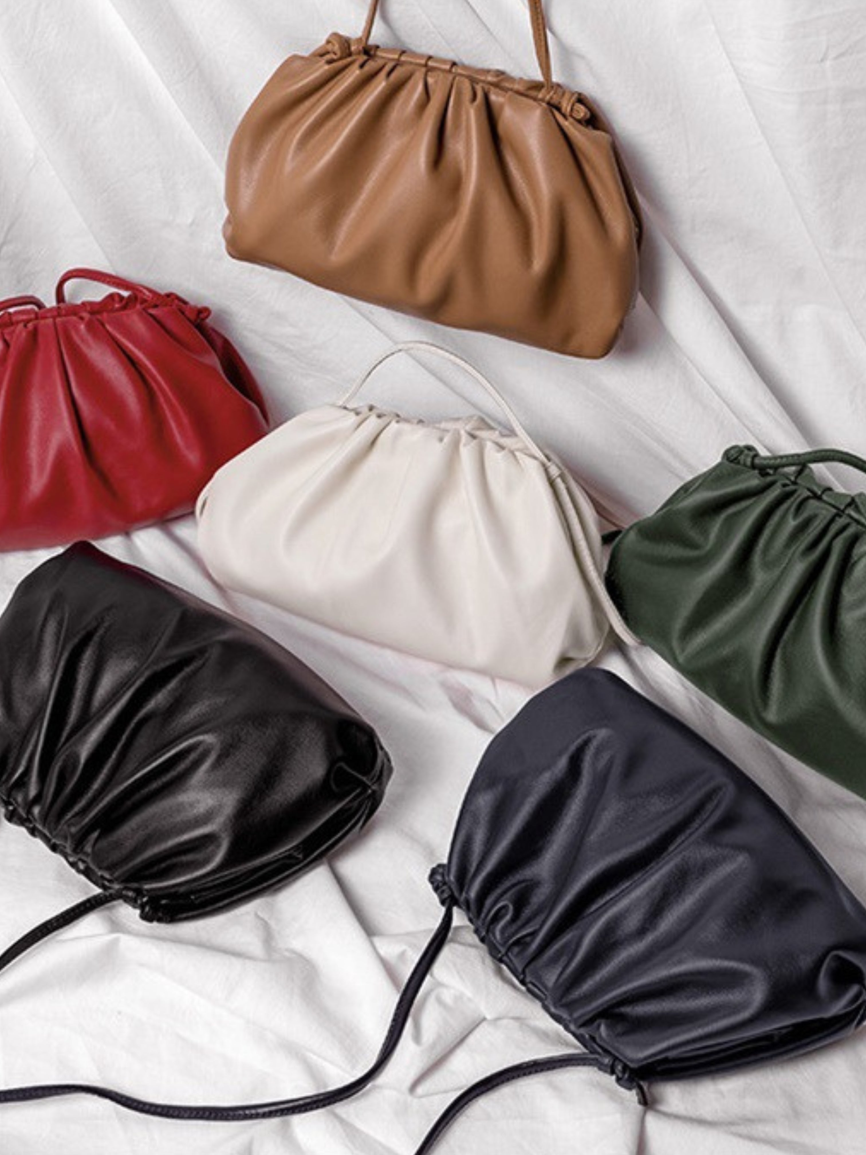 Zes Serena Zachte Leren Pouch Tassen van Liora The Label in bruin, rood, wit, groen, zwart en marineblauw worden getoond op witte stof - elk met een gerimpelde bovenkant en botersoepel leer voor een moderne, luxe uitstraling.