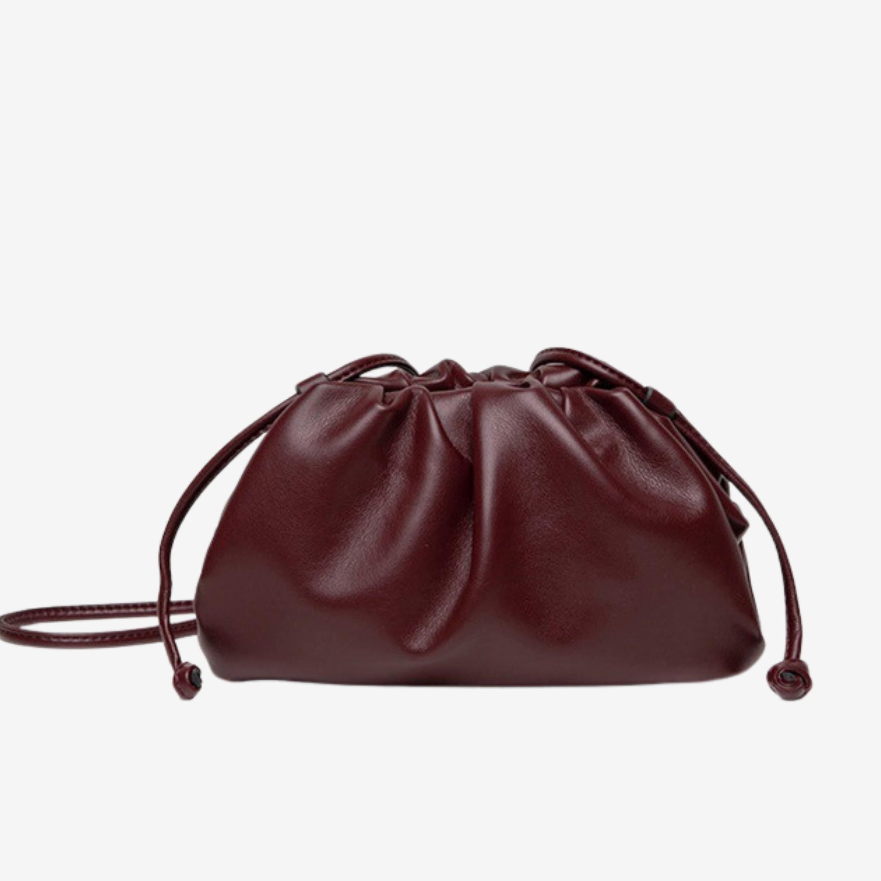 De Serena Zachte Leren Pouch Tas van Liora The Label is een kleine, bordeauxrode tas met een gerimpeld ontwerp en twee trekkoordjes, gemaakt van boterzacht leer, tegen een effen witte achtergrond.