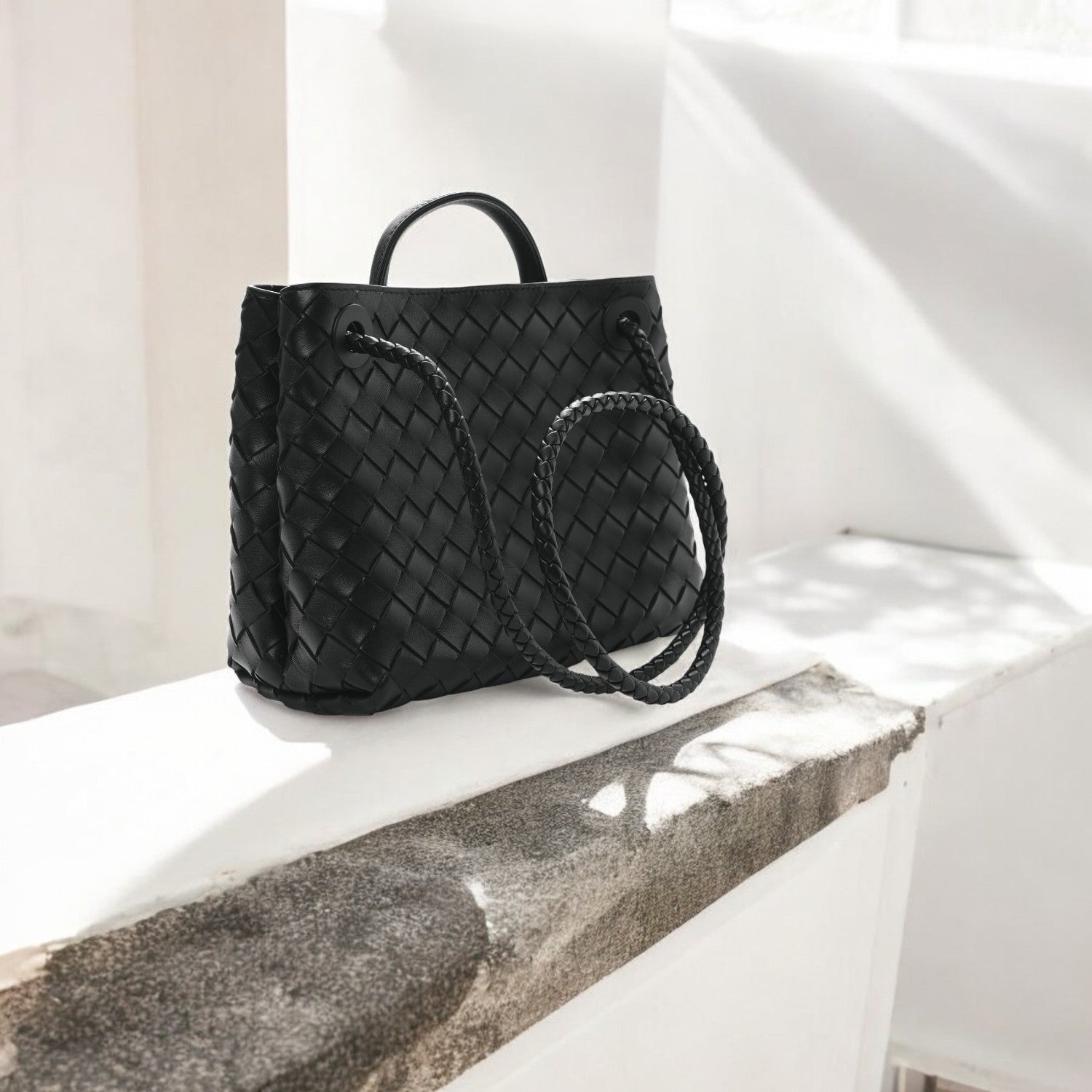 De Alyn Zwarte Geweven Midi Leren Tote Bag van Liora The Label, met korte handvatten en een lange gevlochten schouderriem, straalt moeiteloze elegantie uit-de perfecte luxe tas voor elke handtas dames collectie.