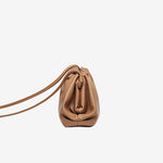 Zijaanzicht van de Serena Zachte Leren Pouch Tas van Liora The Label: een lichtbruine, minimalistische en soepele tas met trekkoordsluiting en dunne schouderbanden, afgebeeld tegen een effen witte achtergrond.
