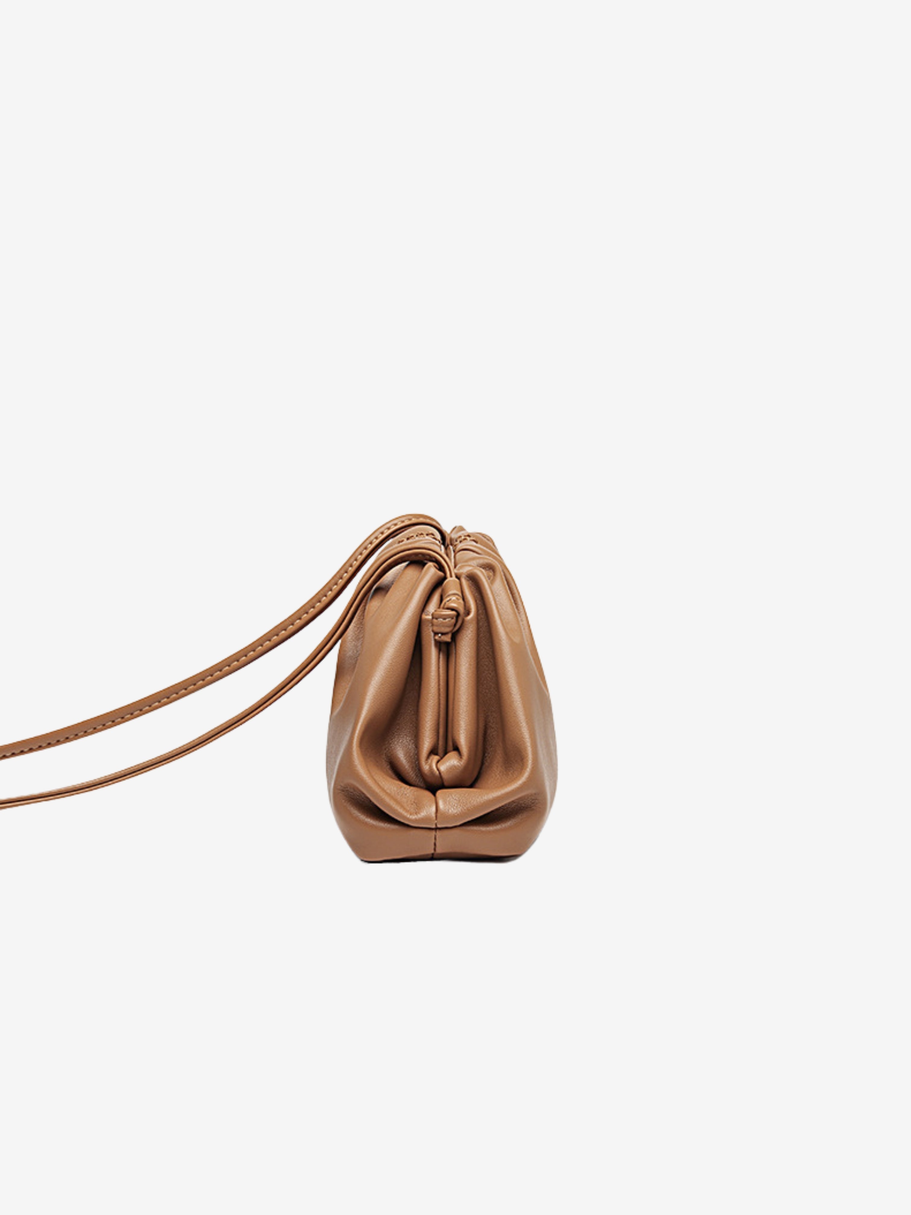 Zijaanzicht van de Serena Zachte Leren Pouch Tas van Liora The Label: een lichtbruine, minimalistische en soepele tas met trekkoordsluiting en dunne schouderbanden, afgebeeld tegen een effen witte achtergrond.