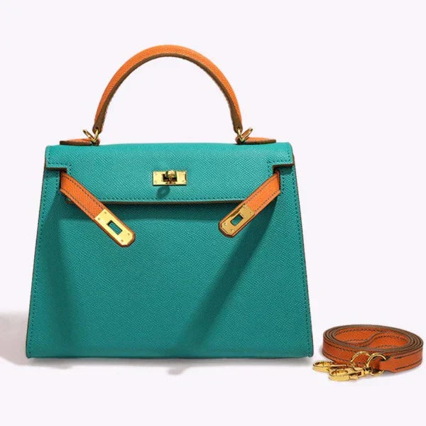 De Jovienne Luxe Teal & Tan Leren Handtas van Liora The Label heeft een handvat aan de bovenkant, contrasterende banden van bruin leer, goudkleurige hardware en een bijpassende afneembare schouderriem, afgebeeld op een lichte achtergrond.