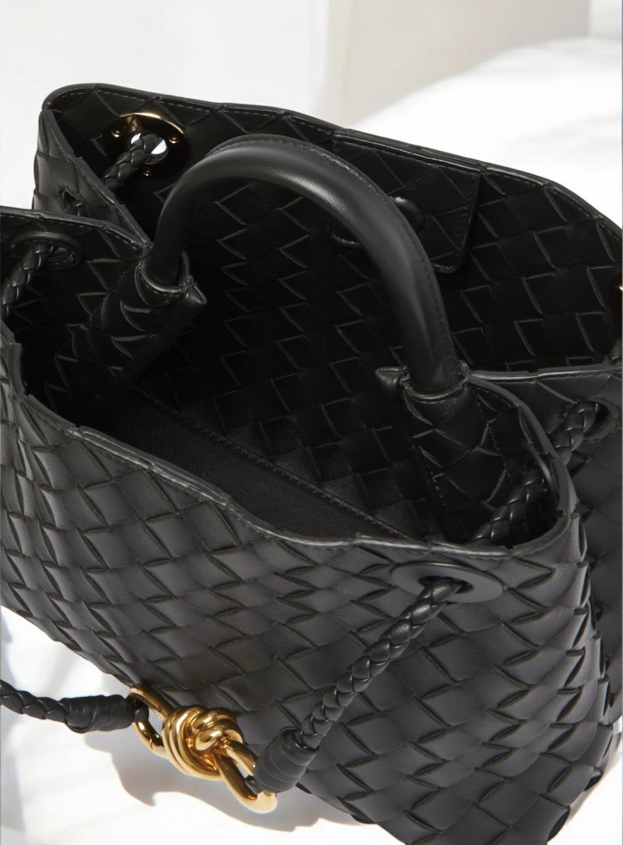 Een close-up van de Alyn Zwarte Geweven Midi Leren Tote Bag van Liora The Label, met gouden hardware en gevlochten hengsels. Deze elegante handtas dames rust op een wit oppervlak, wat de tijdloze uitstraling benadrukt.