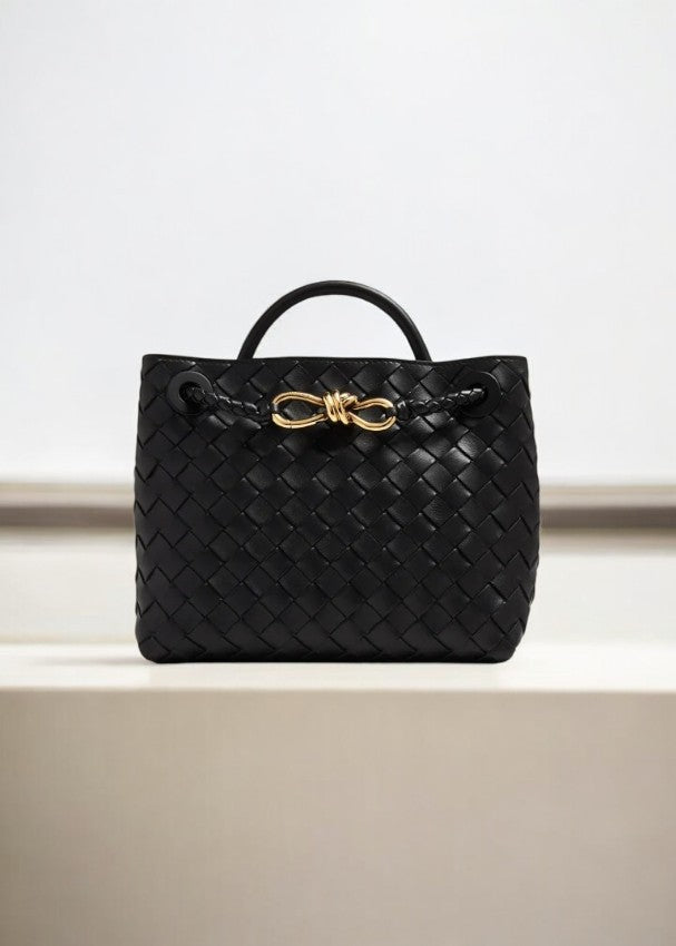 De Alyn zwarte geweven midi leren tote bag van Liora The Label, met korte handgreep en goudkleurige sluiting, straalt moeiteloze elegantie en tijdloze aantrekkingskracht uit. Perfect als luxe handtas voor dames, gepresenteerd tegen een lichte achtergrond.
