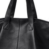 Close-up van de Caro Oversized Leren Tote van Liora The Label, een zwarte minimalistische draagtas met zachte structuur, gemaakt van vegan leer en ontworpen voor dagelijks gebruik, met focus op de handvatten en de textuur.