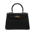 De Galatea handtas van Liora The Label is een elegante, zwarte vegan leren tas met saffiano-textuur, top handvat, goudkleurige details en een draaivergrendeling. Een klassieke mix van luxe en functionaliteit.