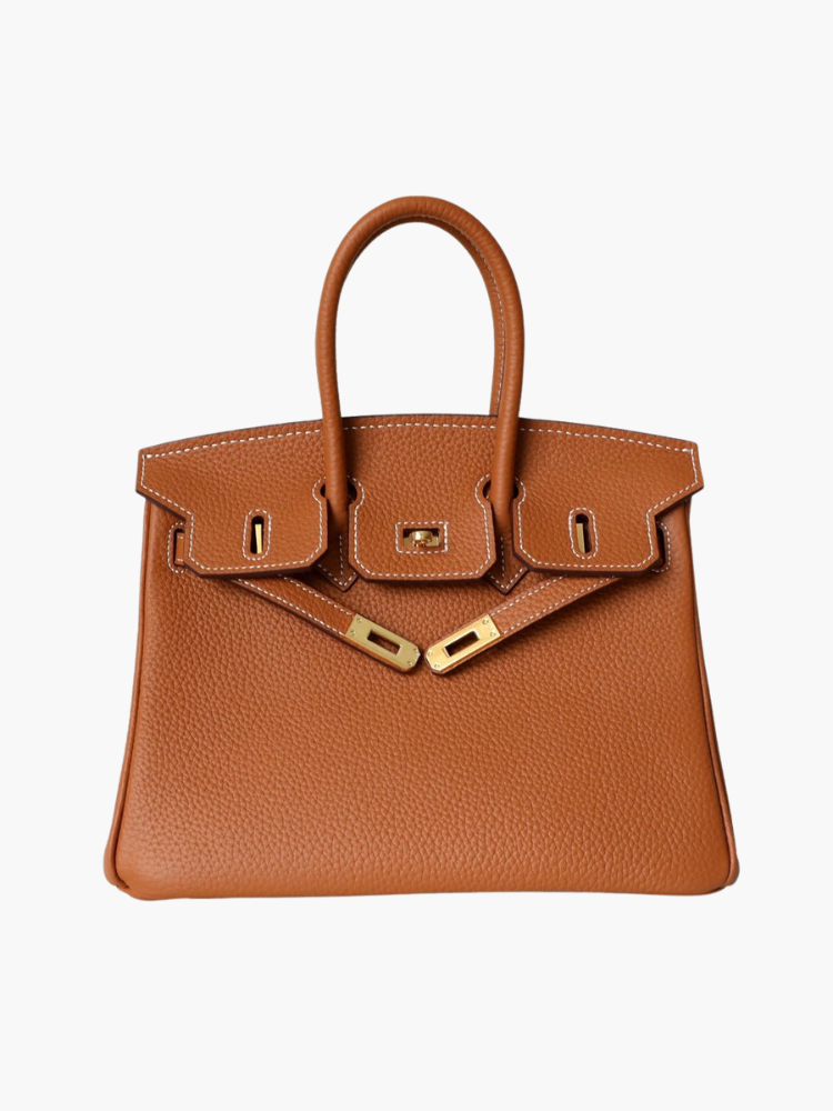 De Isla Tan Textured Leather Handtas van Liora The Label heeft dubbele handvatten, witte stiksels en goudkleurige hardware met slot en sluitingen. Weergegeven op een witte achtergrond voegt deze tas tijdloze elegantie toe aan elke look.
