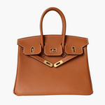 De Isla Tan Textured Leather Handtas van Liora The Label heeft dubbele handvatten, witte stiksels en goudkleurige hardware met slot en sluitingen. Weergegeven op een witte achtergrond voegt deze tas tijdloze elegantie toe aan elke look.