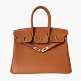 De Isla Tan Textured Leather Handtas van Liora The Label heeft dubbele handvatten, witte stiksels en goudkleurige hardware met slot en sluitingen. Weergegeven op een witte achtergrond voegt deze tas tijdloze elegantie toe aan elke look.