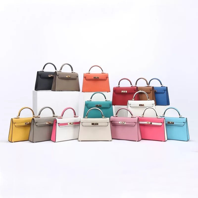 Een set van 15 Aurora Signature Mini Leren Handtassen van Liora The Label in geel, grijs, rood, oranje, blauw, wit, roze, groenblauw en bruin volnerfleer gerangschikt in drie rijen op een witte achtergrond.