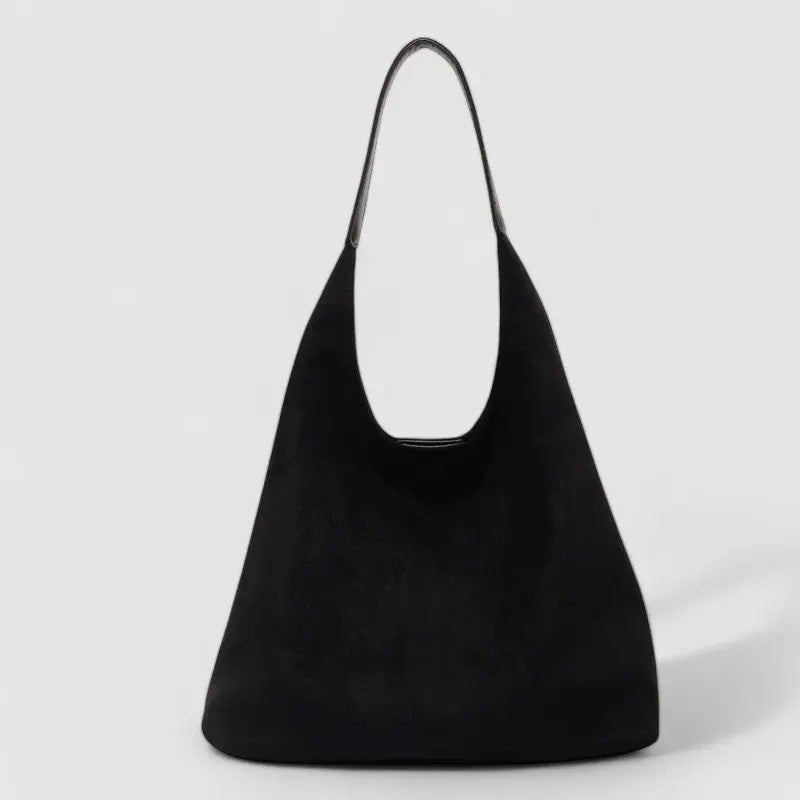 De Lena Minimalistische Suède Hobo Tas van Liora The Label is een zwarte veganistische suède tas met een brede, ronde body en enkele riem, afgebeeld op een effen lichtgrijze achtergrond.