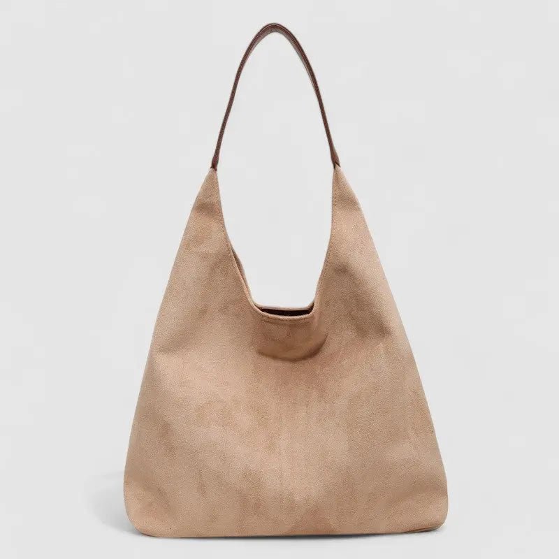 De Lena Minimalistische Suède Hobo Tas van Liora The Label is een grote, zachtbeige veganistische suède tas met een enkele schouderriem, rechtopstaand afgebeeld tegen een effen lichtgrijze achtergrond.