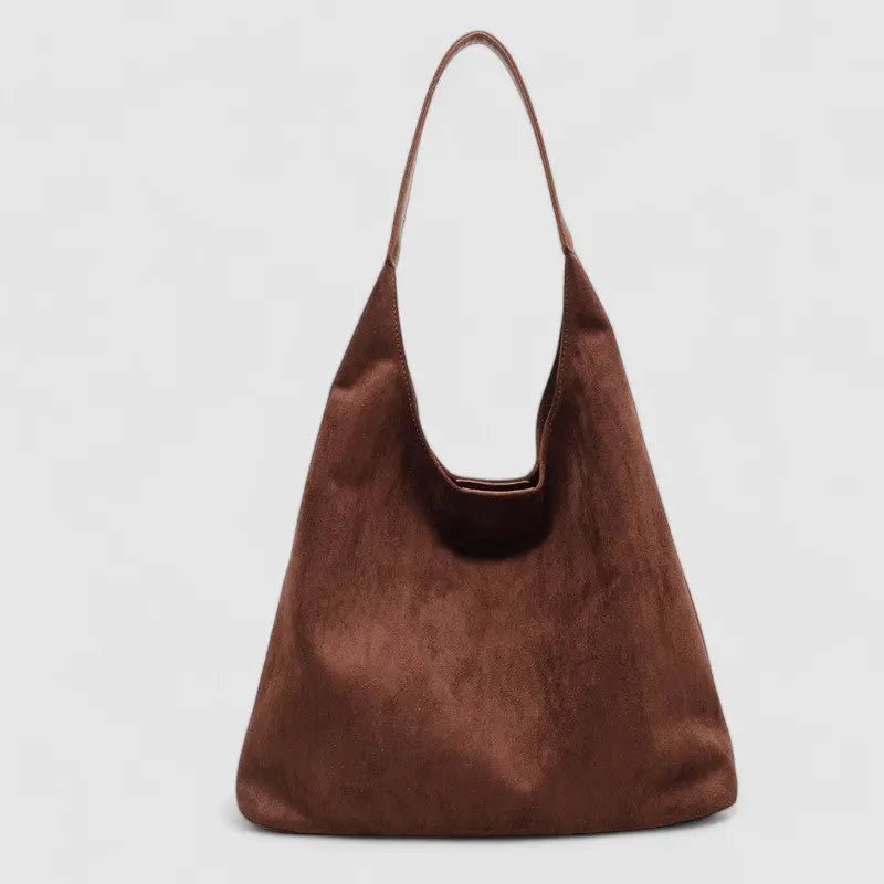 De Lena Minimalistische Suède Hobo Tas van Liora The Label, in bruin vegan suède met een slouchy driehoekige vorm en enkele band, straalt moeiteloze elegantie en functionaliteit uit tegen een lichtgrijze achtergrond.