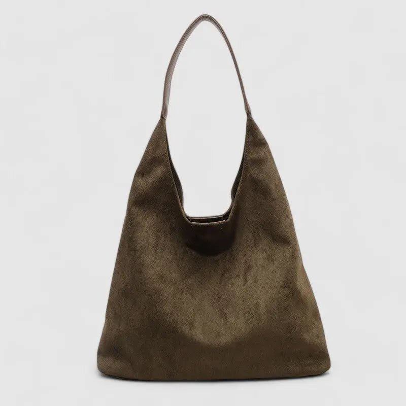 De Lena minimalistische suède hobo tas van Liora The Label is een luxe dames handtas in bruin met één schouderband, moeiteloos elegant en functioneel, gefotografeerd tegen een effen lichtgrijze achtergrond.