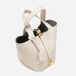 De Elaris | Luxe Taupe Leren Emmer Tas van Liora The Label heeft goudkleurige hardware, ritssluiting, twee handgrepen en een gestructureerde emmervorm. Het elegante taupe leer steekt af tegen een effen witte achtergrond.