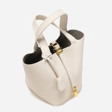 De Elaris | Luxe Taupe Leren Emmer Tas van Liora The Label heeft goudkleurige hardware, ritssluiting, twee handgrepen en een gestructureerde emmervorm. Het elegante taupe leer steekt af tegen een effen witte achtergrond.