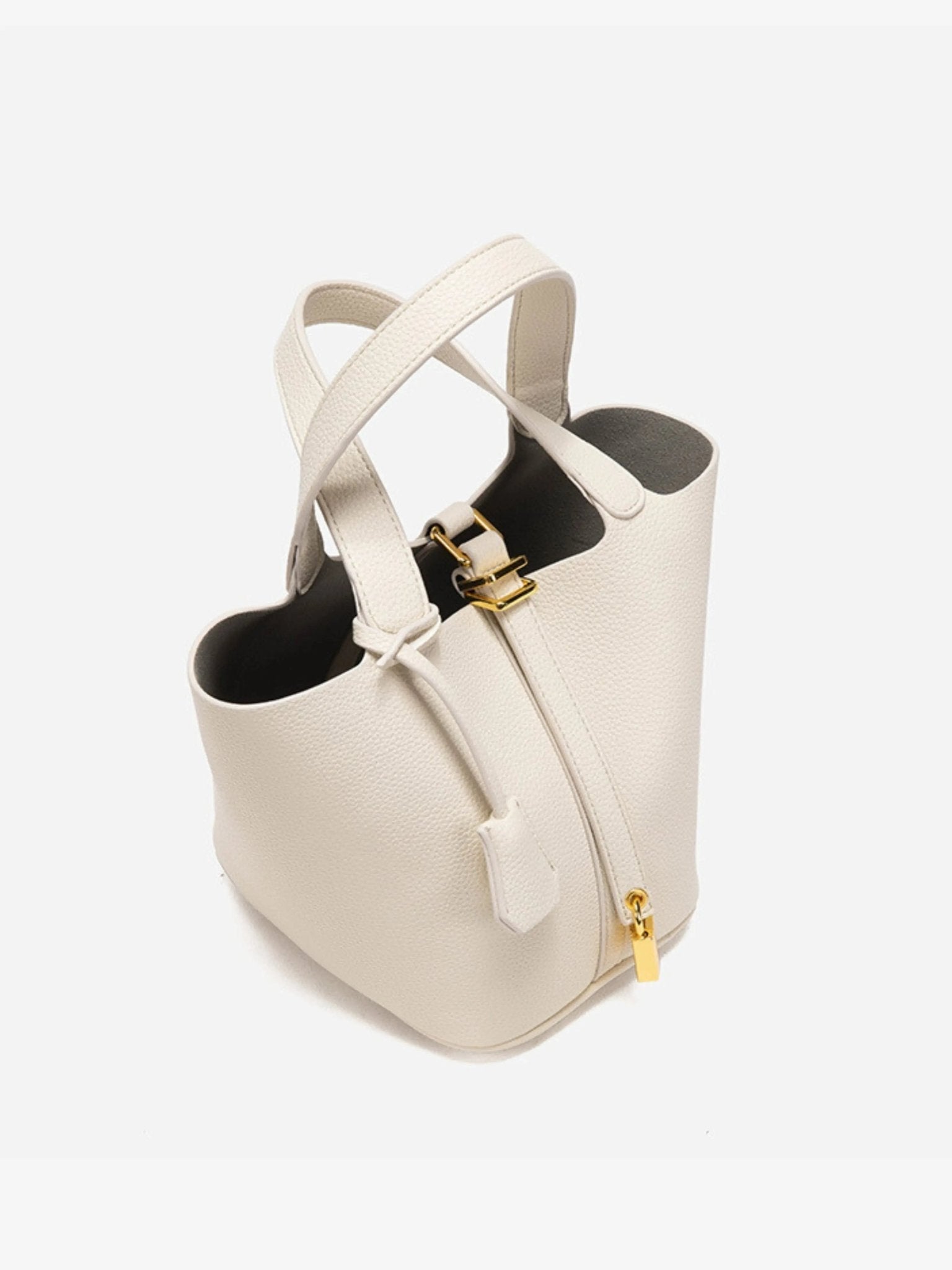 De Elaris | Luxe Taupe Leren Emmer Tas van Liora The Label heeft goudkleurige hardware, ritssluiting, twee handgrepen en een gestructureerde emmervorm. Het elegante taupe leer steekt af tegen een effen witte achtergrond.