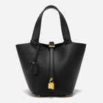 De Elaris Luxe Taupe Leren Emmer Tas van Liora The Label heeft eersteklas structuurleer, twee handgrepen, een goudkleurige hangslotsluiting en een bijpassende leren sleutelhouder-elegant weergegeven tegen een effen witte achtergrond.