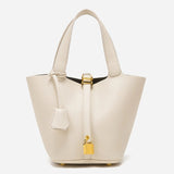 De Elaris Luxe Taupe Leren Emmer Tas van Liora The Label is een eersteklas, crèmekleurige bucket bag met twee bovenhengsels en een gouden hangslotdetail, afgebeeld tegen een effen witte achtergrond.