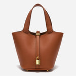 De Elaris | Luxe Taupe Leren Emmer Tas van Liora The Label is een tijdloze, elegante bucket bag met gekiezeld leer, twee hengsels en een gouden gesp, tegen een effen witte achtergrond.