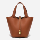 De Elaris | Luxe Taupe Leren Emmer Tas van Liora The Label is een tijdloze, elegante bucket bag met gekiezeld leer, twee hengsels en een gouden gesp, tegen een effen witte achtergrond.