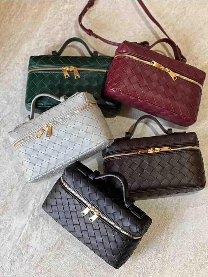 Vijf luxe Geweven Box Tassen van Liora The Label, waaronder een elegante donkerbruine crossbody met gouden ritssluiting, worden getoond op een licht oppervlak. Elke tas heeft een veganistische leer met slotdetail en een bovenhandgreep voor tijdloze allure.