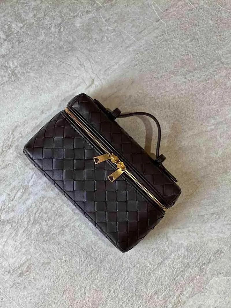 De Luxe Geweven Box Bag van Liora The Label is een elegante donkerbruine crossbody met gouden ritssluiting, getoond op een licht getextureerd oppervlak.