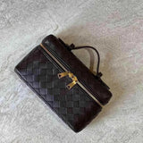 De Luxe Geweven Box Bag van Liora The Label is een elegante donkerbruine crossbody met gouden ritssluiting, getoond op een licht getextureerd oppervlak.