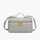 De Luxe Geweven Box Bag van Liora The Label is een kleine, rechthoekige, donkerbruine crossbody van veganistisch leer met gouden ritssluiting, gouden hardware, handvat aan de bovenkant en verstelbare schouderriem.