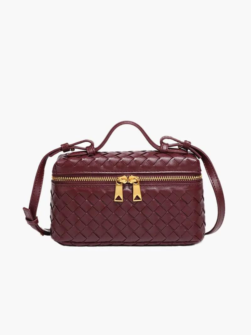 De Luxe Geweven Box Bag van Liora The Label is een elegante donkerbruine crossbody met een gouden ritssluiting, bovenhandgreep en verstelbare schouderriem, afgebeeld op een witte achtergrond.